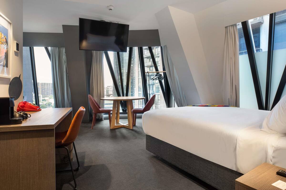 Ett hotellrum med en säng, ett skrivbord, en stol och en tv.