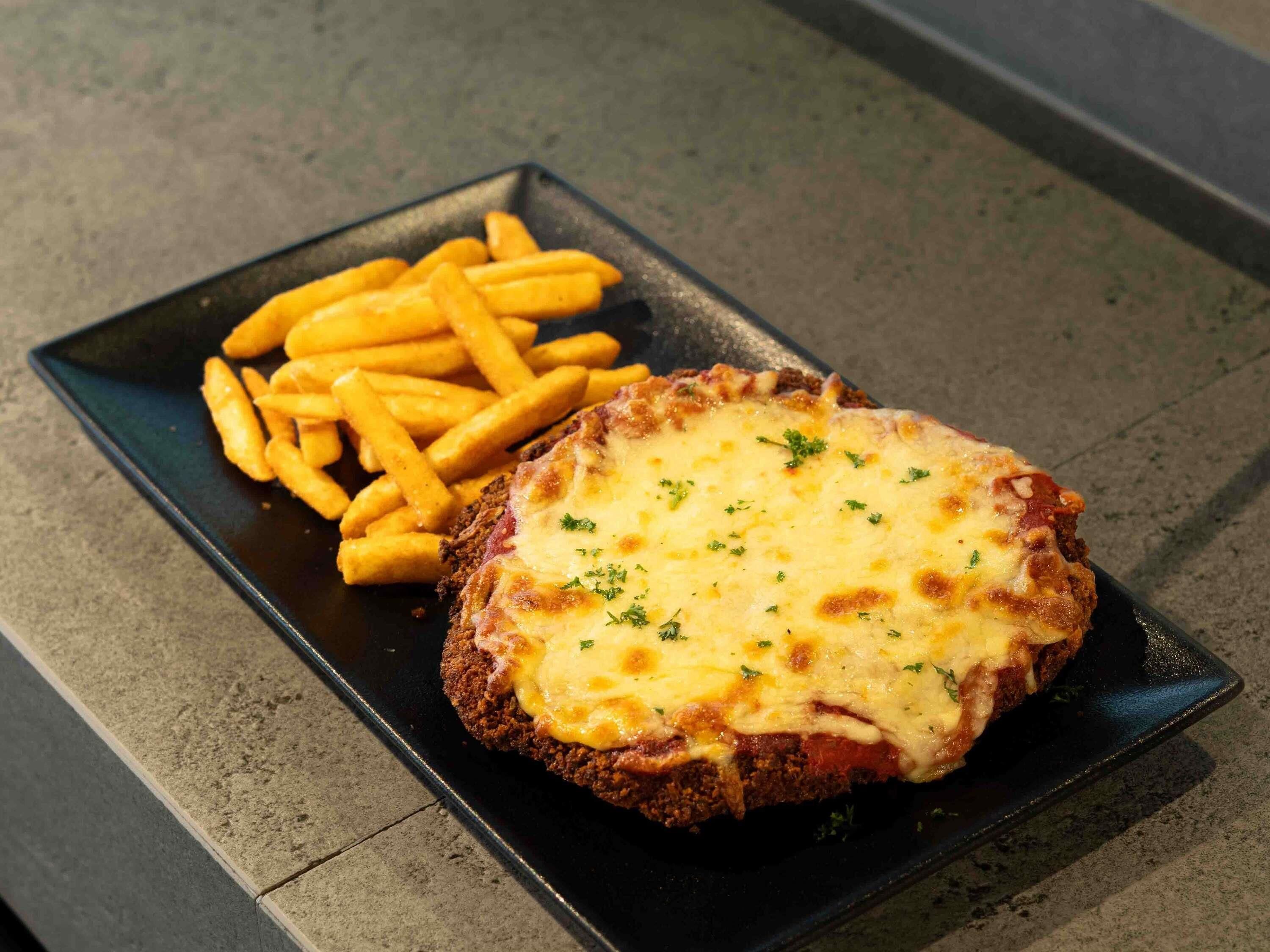 A black rectangular plate with a breaded item topped with melted cheese and a side of French fries.