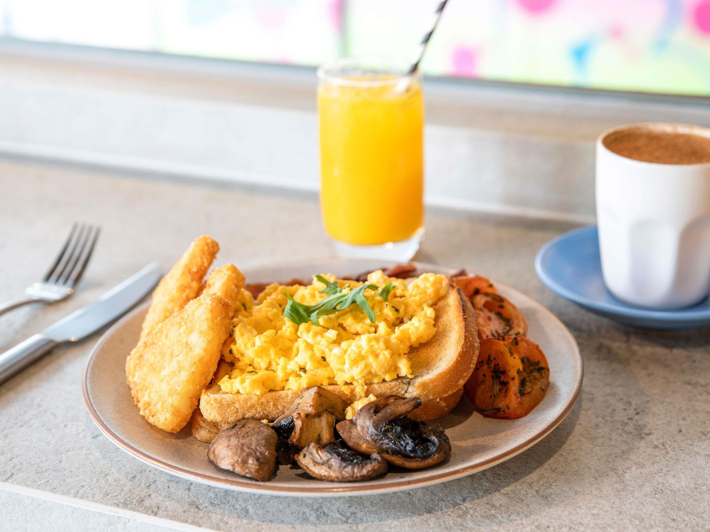 Un plato de desayuno con huevos revueltos, champiñones, tostadas y un vaso de jugo de naranja.
