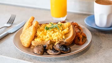 Un plato de desayuno con huevos revueltos, champiñones, tostadas y un vaso de jugo de naranja.