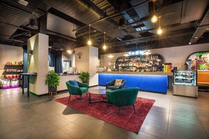 Un espacio de bar con mostrador, dos sillas verdes, un tapete rojo y una vitrina.
