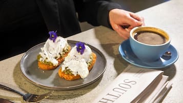 A plate with two food items topped with cream and purple flowers, a cup of coffee, and a menu on a table.