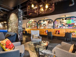 Un espacio lounge moderno con asientos, una barra de café y una pared decorada con carteles de eventos.