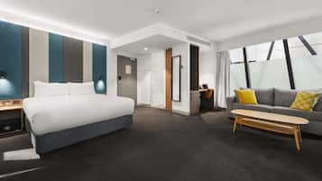 Una habitación de hotel moderna con cama, sofá, escritorio y ventana grande.