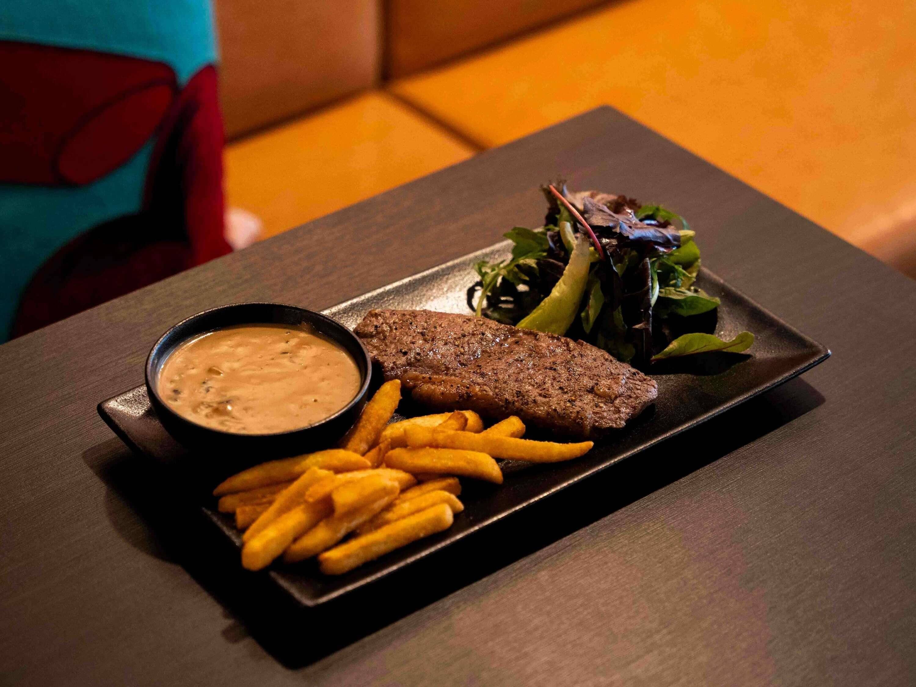 Une assiette contenant un steak, des frites et une salade, posée sur une table sombre.