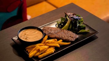Une assiette contenant un steak, des frites et une salade, posée sur une table sombre.
