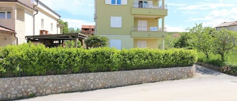 Um edifício residencial com vários andares, varandas, um muro de pedra e um acesso pavimentado.