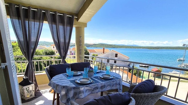 A balcony with a table set for two, wicker chairs, and a view of the sea. - Apartment Sonja (Klimno - island Krk)