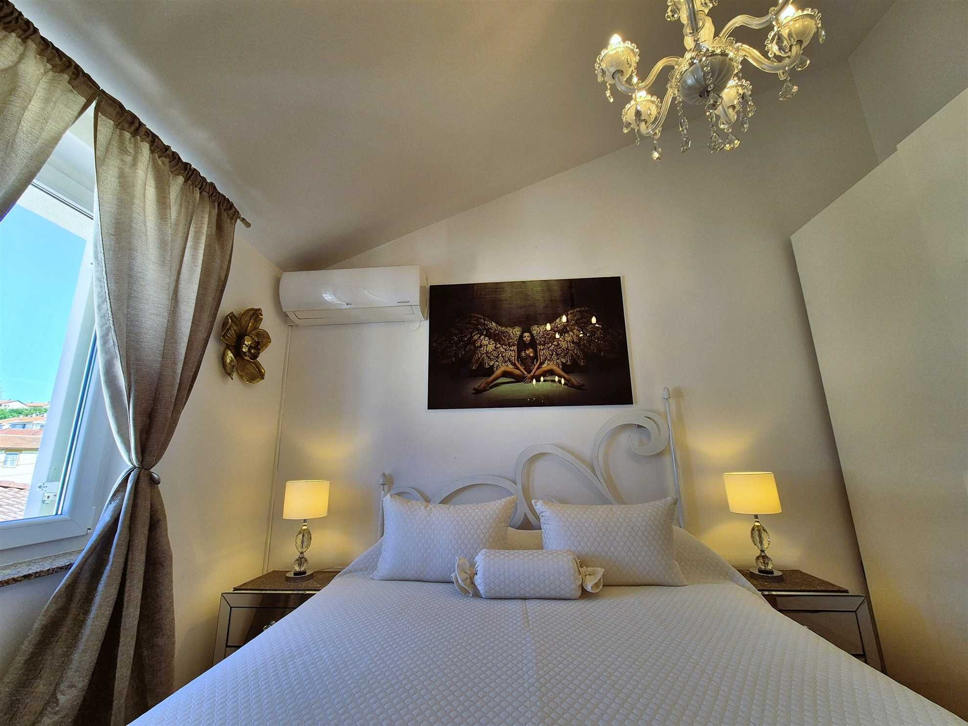 Une chambre d’hôtel avec un grand lit, deux tables de chevet avec des lampes, un climatiseur fixé au mur et un lustre.