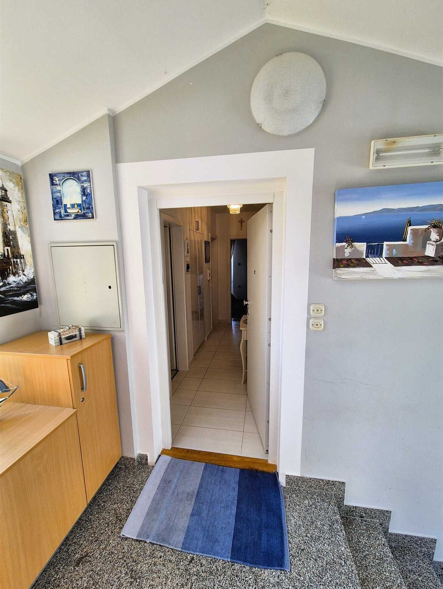A hallway leading to a bedroom with a view, a wooden desk, a painting, and a small rug.