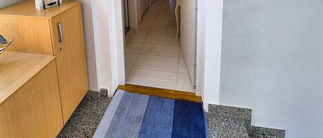 A hallway leading to a bedroom with a view, a wooden desk, a painting, and a small rug.