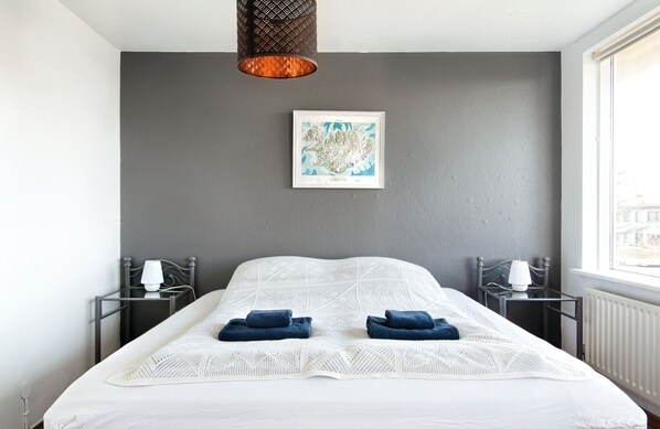 Une chambre d’hôtel moderne avec un grand lit, deux tables de chevet avec des lampes, une carte encadrée accrochée au mur et une vue sur la ville par la fenêtre.