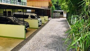 Un espace de stationnement avec plusieurs voitures, un chemin de gravier et un bâtiment à la façade verte.