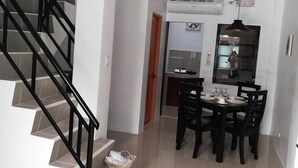 Un intérieur moderne avec un escalier, un coin repas comprenant une table et des chaises, et une cuisine visible à travers une porte ouverte.