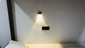 A neatly made bed with white linens and a folded towel, a wall-mounted light fixture, and a power outlet on a plain wall. - Backpackers Villa (Arugam Bay)