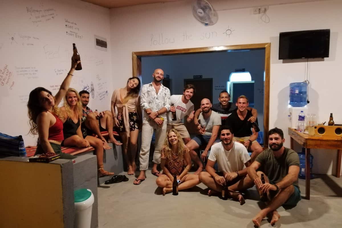 A group of people in a room with a whiteboard, a fan, and a television on the wall.