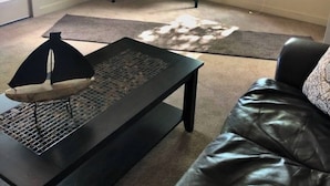 A living room with a black leather couch, a coffee table, a television on a stand, a rug, and a door.