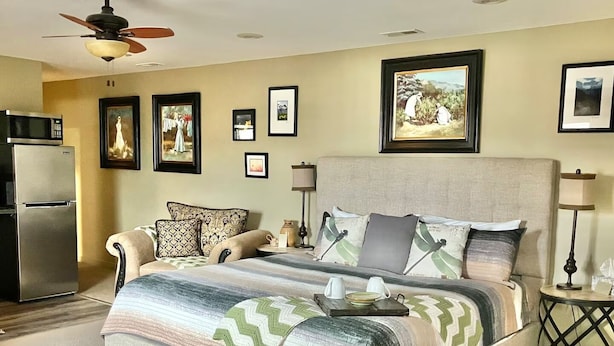 A bedroom with a bed, a sofa, a refrigerator, a lamp, and framed pictures on the wall.