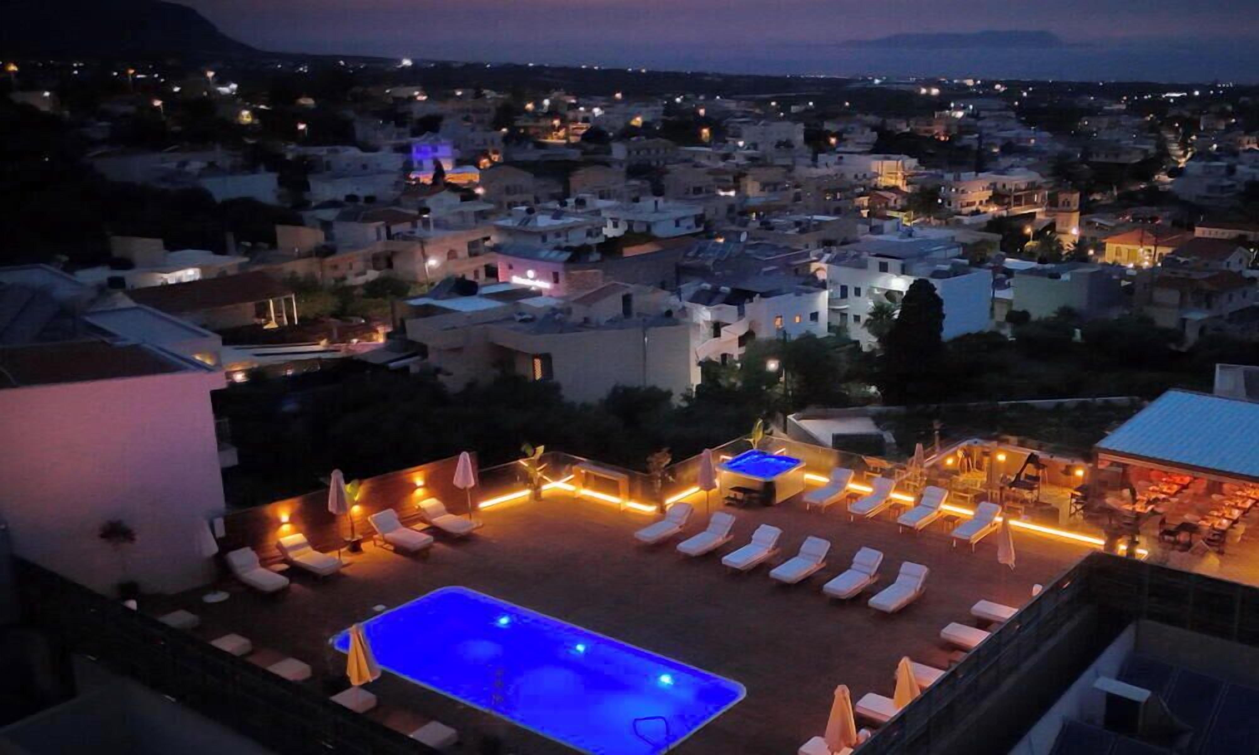 Zona de piscina en la azotea con sillones de descanso y un jacuzzi, rodeada de edificios.