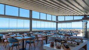 A spacious dining area with large windows, wooden tables, and chairs, and a buffet with various food items.