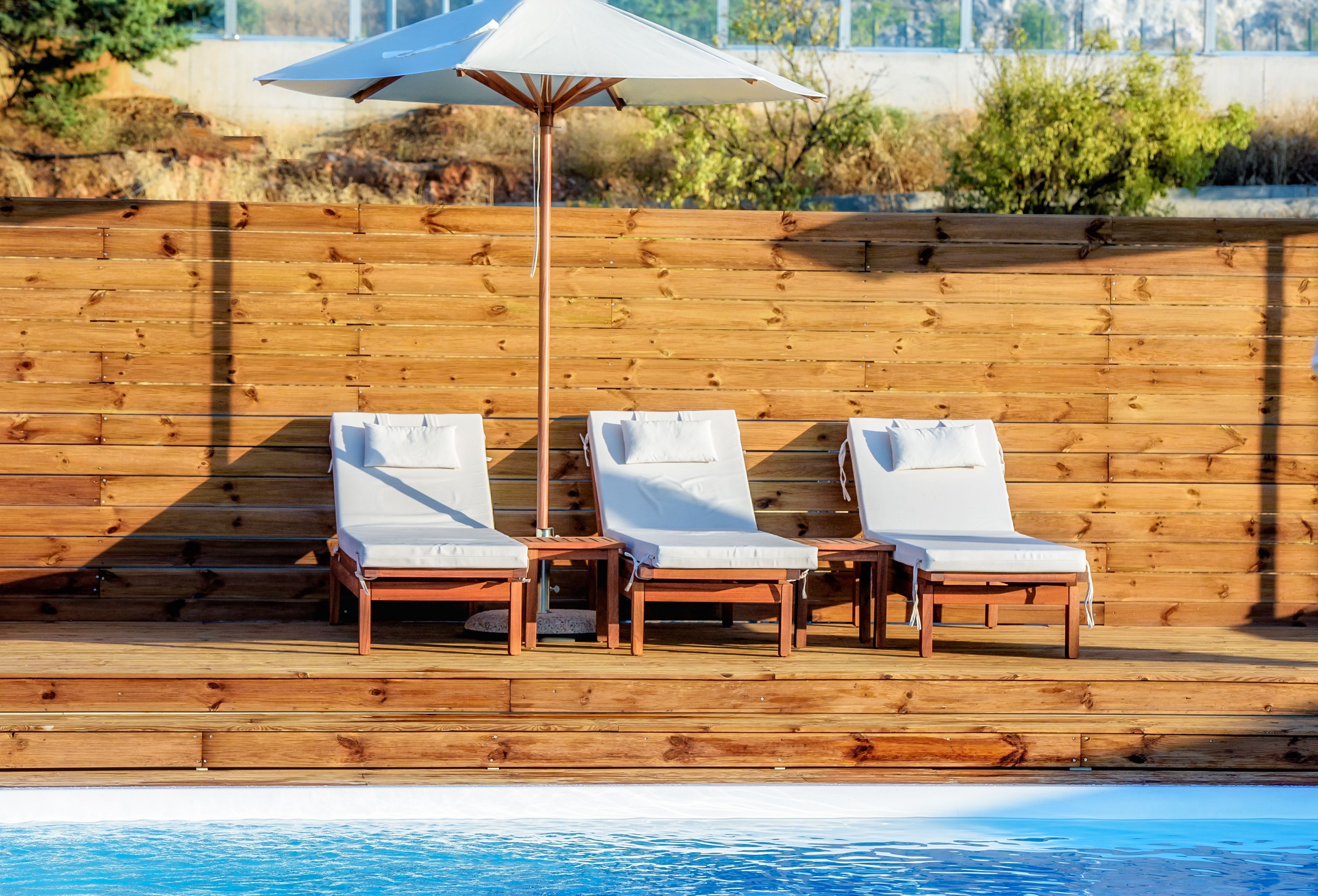 Una terraza de madera con tres sillones blancos y una sombrilla blanca.