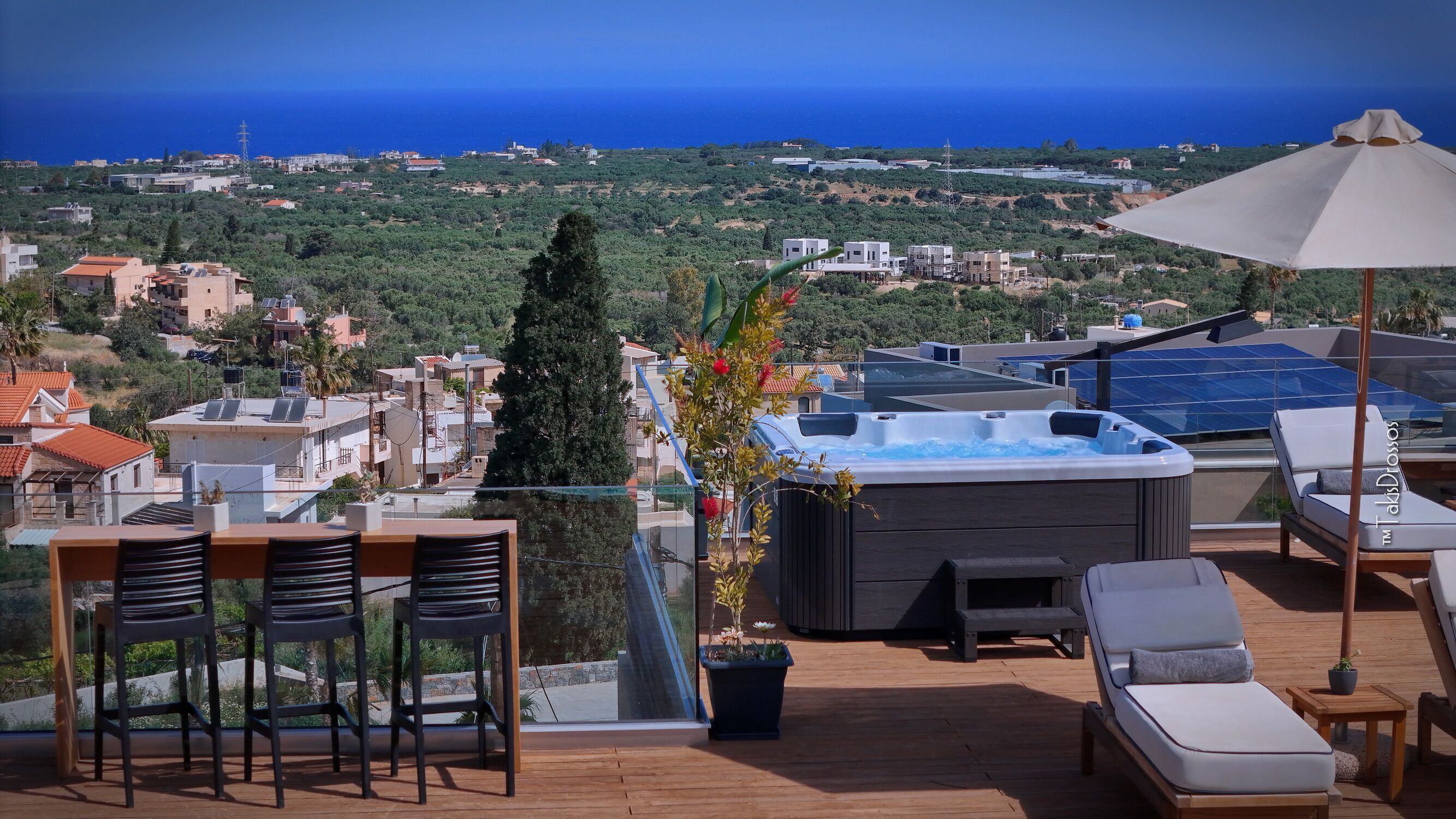 A rooftop terrace with a hot tub, lounge chairs, and a view of the sea and surrounding buildings.