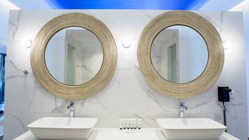 A bathroom with two sinks, each with a large round mirror above. The walls are white marble, and there is a ceiling light fixture.