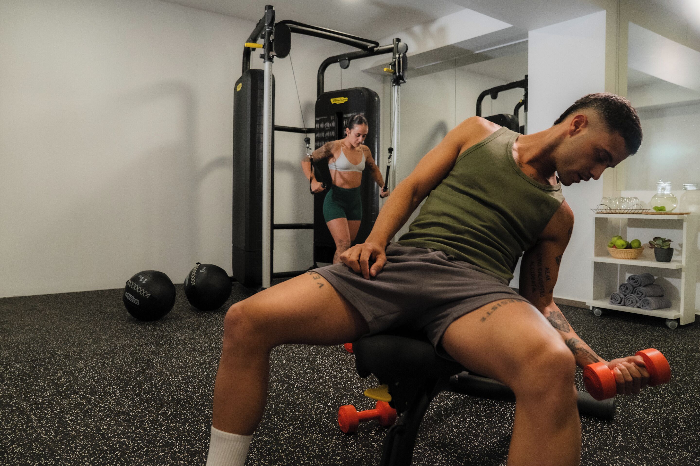 A gym with exercise equipment, a person using a leg press machine, and another person in the background.