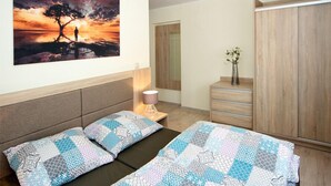 Une chambre à coucher comprenant un lit, une table de chevet, une lampe, une armoire et un tableau représentant un arbre au bord de l’eau.