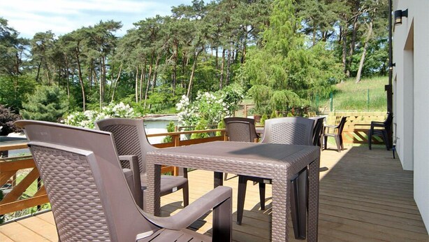 Une terrasse dotée d’une table et de chaises, entourée d’une rambarde en bois, et offrant une vue sur une zone boisée.