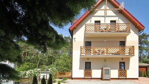 Un bâtiment à deux étages, doté d’un toit rouge, de balcons en bois et d’un chemin de pierre menant à l’entrée.