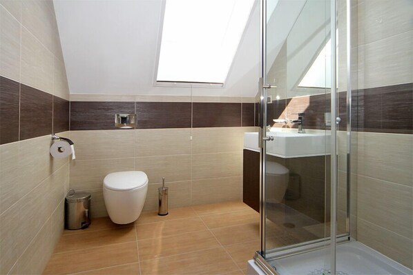 Un baño moderno con tragaluz, inodoro, cubo de basura y cabina de ducha de vidrio.