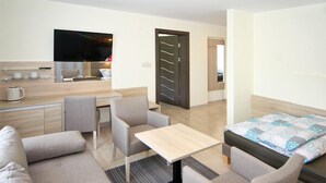 Une chambre d’hôtel moderne équipée d’un canapé, d’une petite table, d’une télévision, d’un coin cuisine et d’un lit avec une couette.