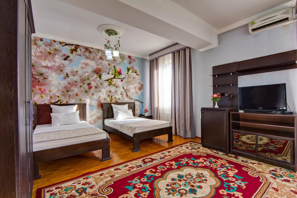 Una habitación de hotel con dos camas individuales, televisión, un amplio mural floral en la pared y una alfombra roja estampada.
