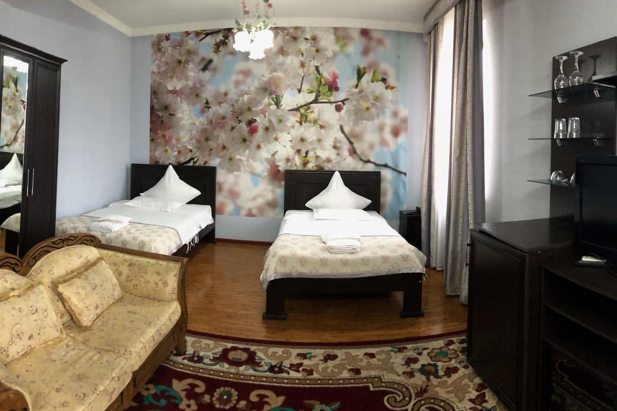 Habitación de hotel con dos camas, un sofá, un televisor y un mural floral en la pared.