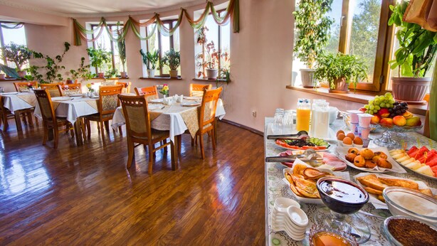 A dining area with multiple tables and chairs, a buffet with various food items, and potted plants near the windows. - King House hotel (Bishkek)
