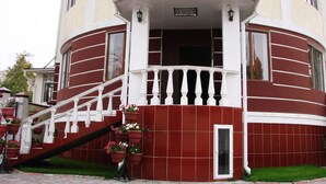 A multi-story building with a red and white facade, a central entrance with a white balustrade, and a staircase leading to the entrance. - King House hotel (Bishkek)