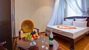 A hotel room with a bed, a dining table with fruit and wine glasses, and a chair. - King House hotel (Bishkek)