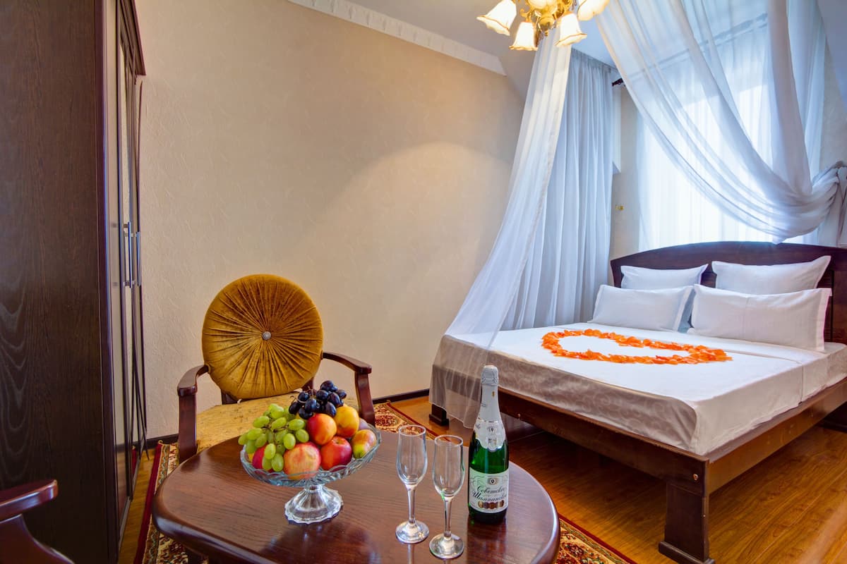 Habitación de hotel con cama, una mesa de comedor con fruta y copas de vino, y una silla.
