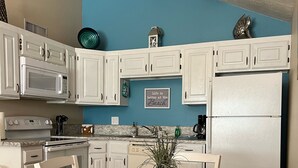Une cuisine avec des meubles blancs, un mur bleu, une table à manger avec des chaises et une plante en pot.