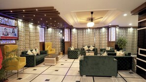 A modern lobby with a mix of sofas and armchairs, a ceiling fan, and patterned curtains. - Hotel Bhawani International (Reasi)