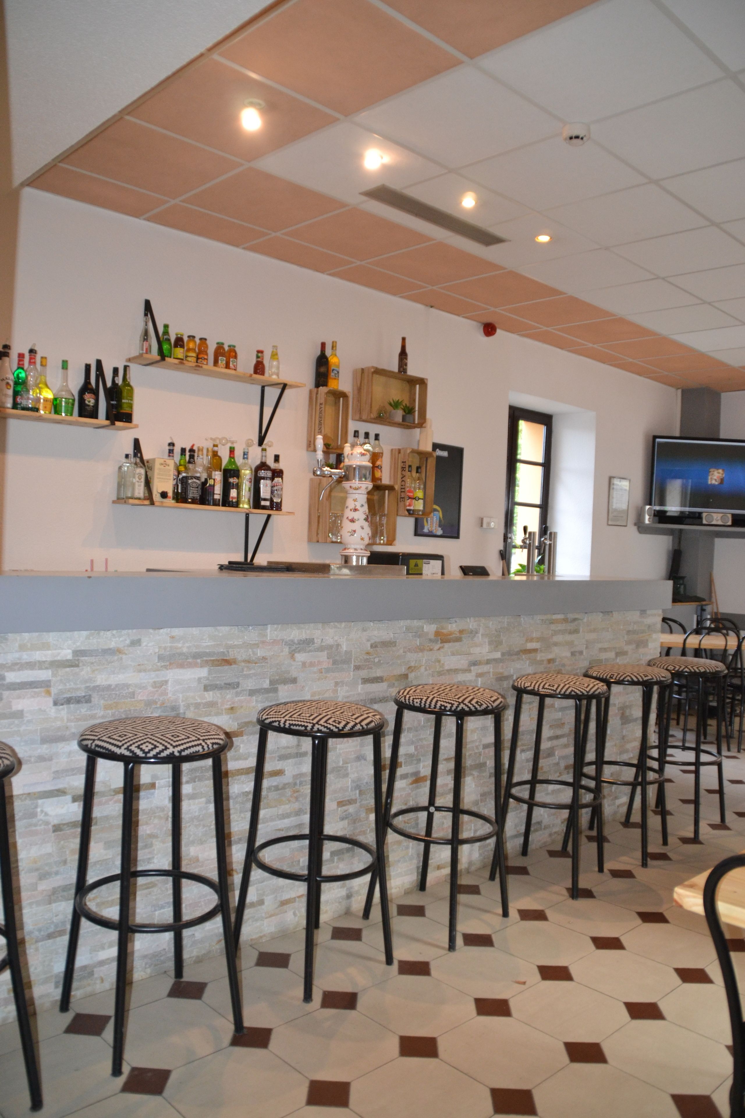 A bar area with stools, a counter, and shelves with bottles.
