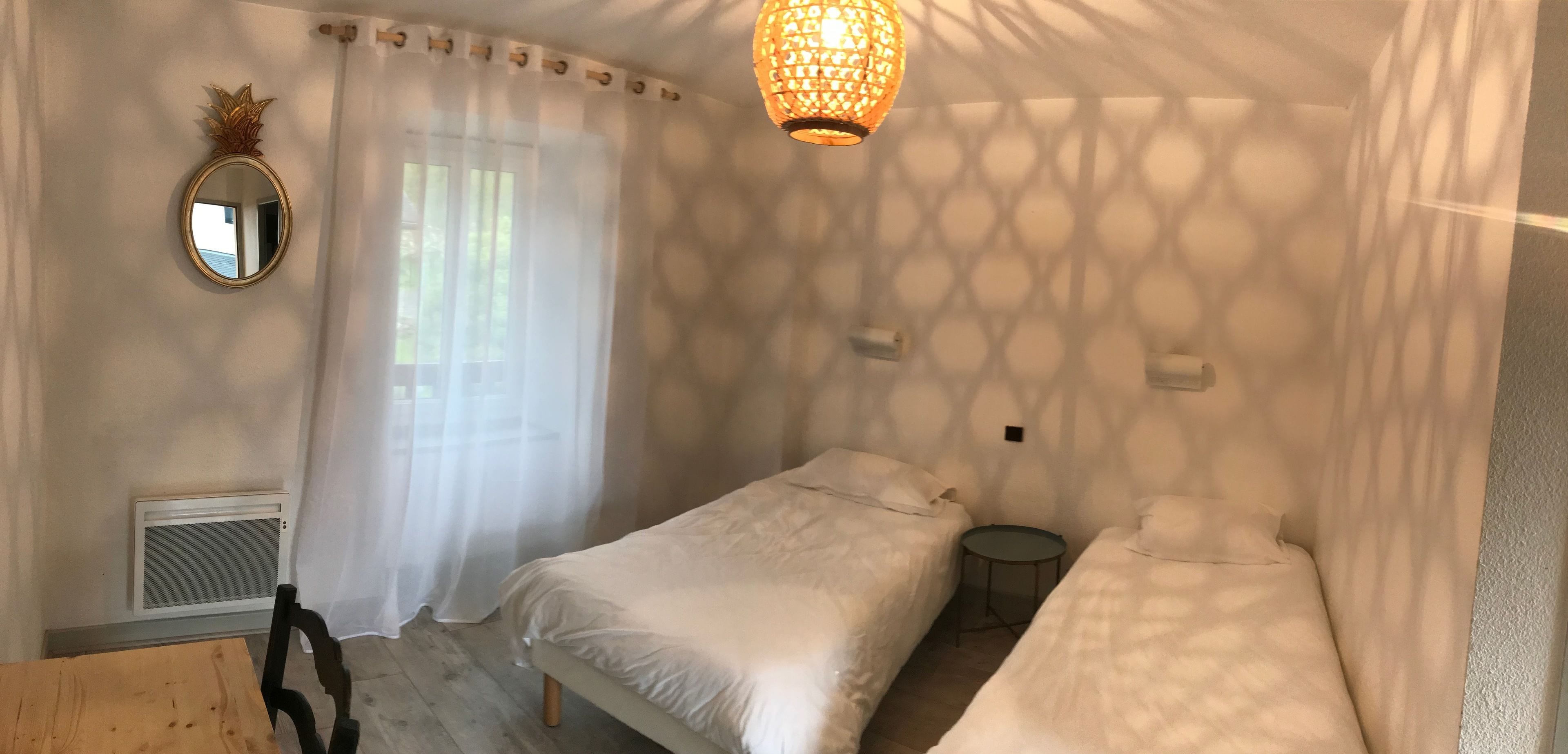 A bedroom with two beds, a round table, a mirror, and a ceiling light fixture.