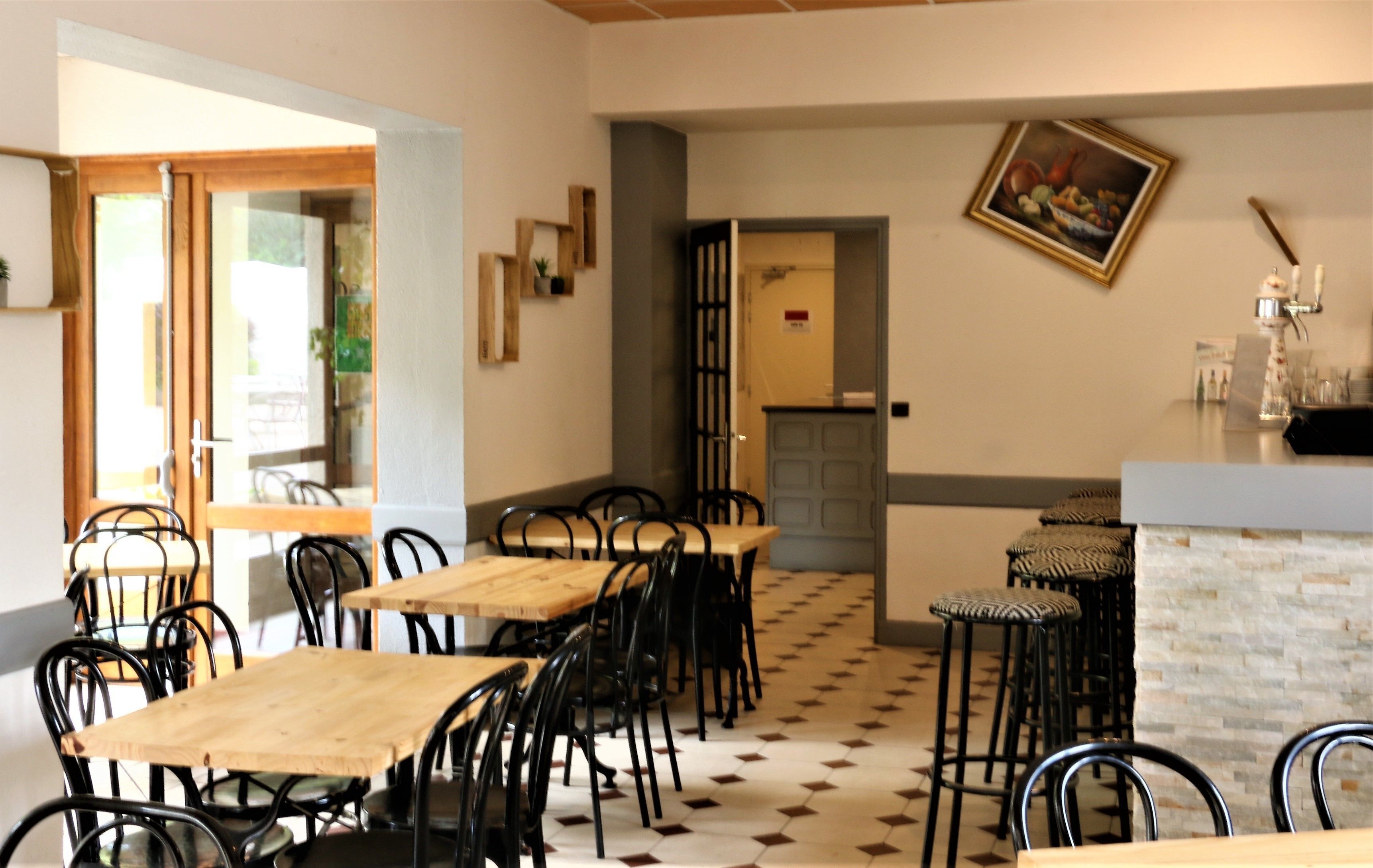 A restaurant with wooden tables and black chairs, a tiled floor, and a painting on the wall.