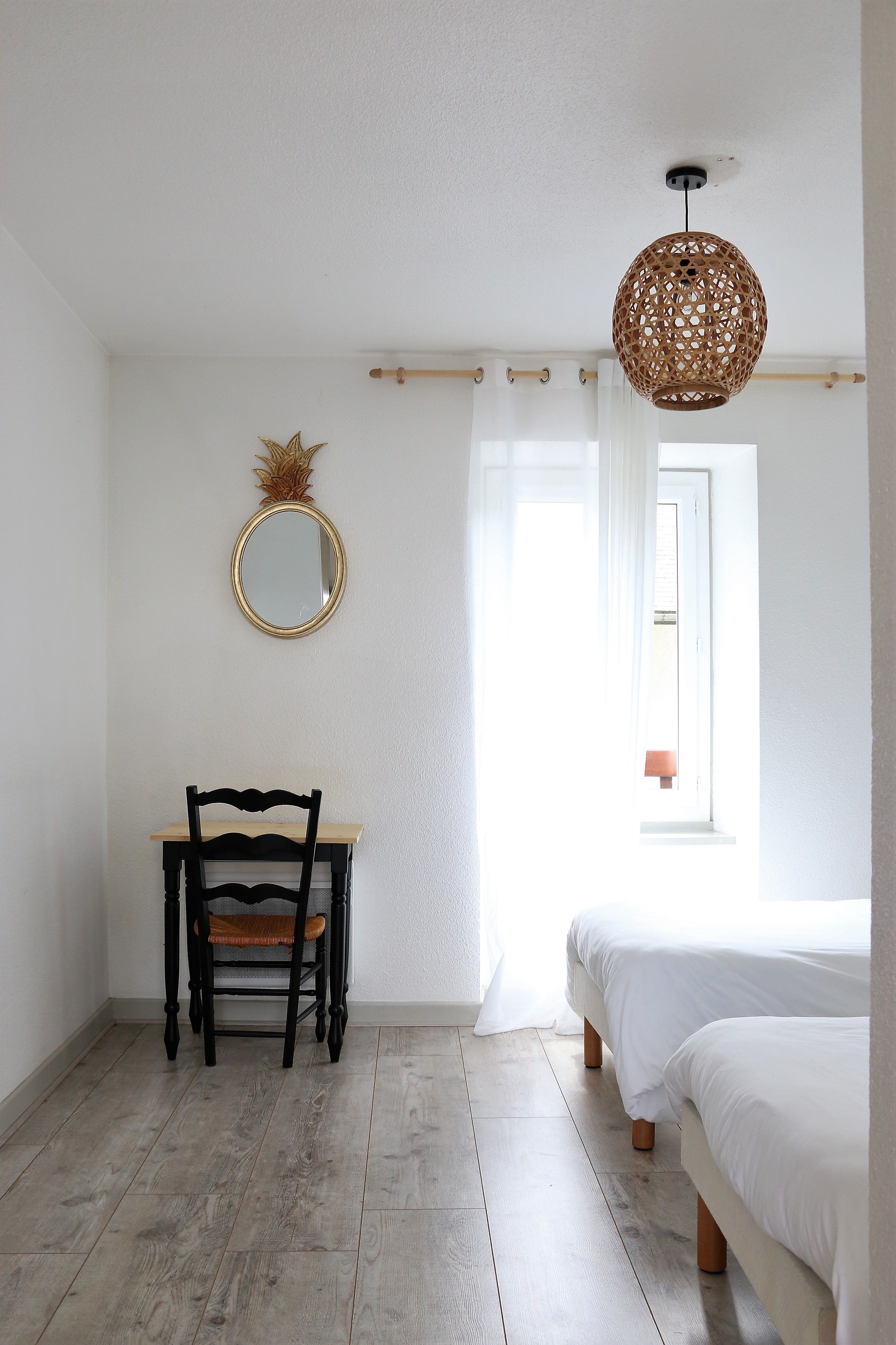 A bedroom with a bed, a chair, a desk, a mirror, and a hanging light fixture.