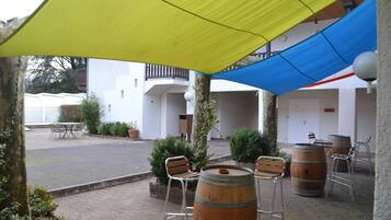 An outdoor patio with wooden barrels, metal chairs, and a yellow and blue canopy.