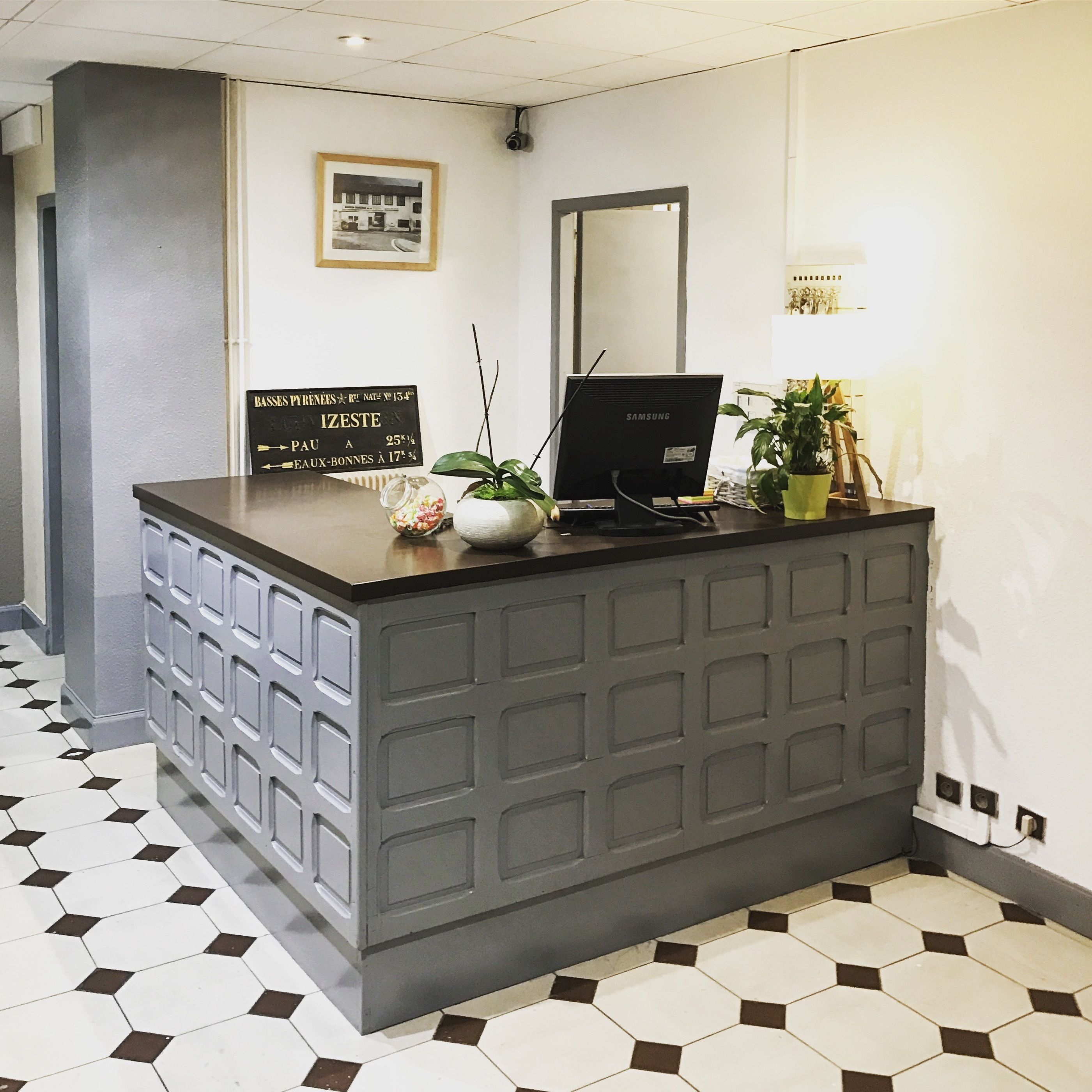 A reception desk with a computer, a framed sign, and a potted plant.