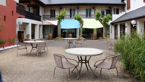 Une cour avec des sièges en plein air, un bâtiment doté de balcons et un espace couvert agrémenté de parasols.