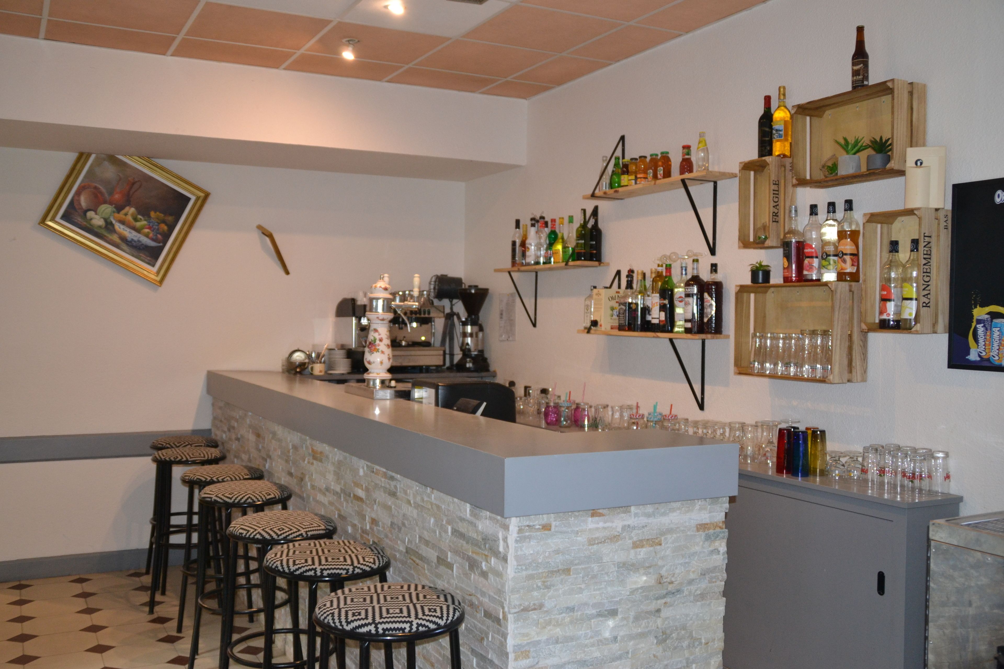 A bar area with stools, a counter, and shelves with bottles and glasses.