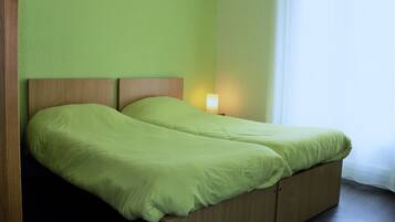 A double bed with a wooden headboard and a green bedspread. There is a bedside table with a lamp on it.